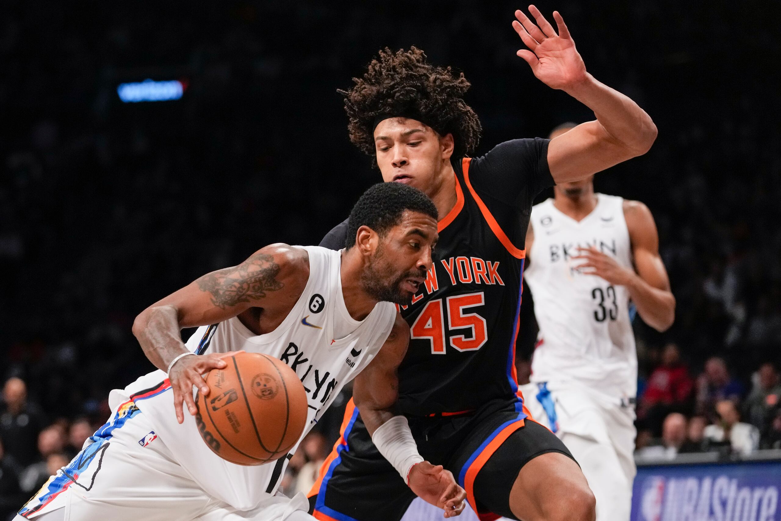 El armador de los Nets de Brooklyn, Kyrie Irving, inicia movimientos contra el centro de los Knicks, Jericho Sims durante el partido sabatino.