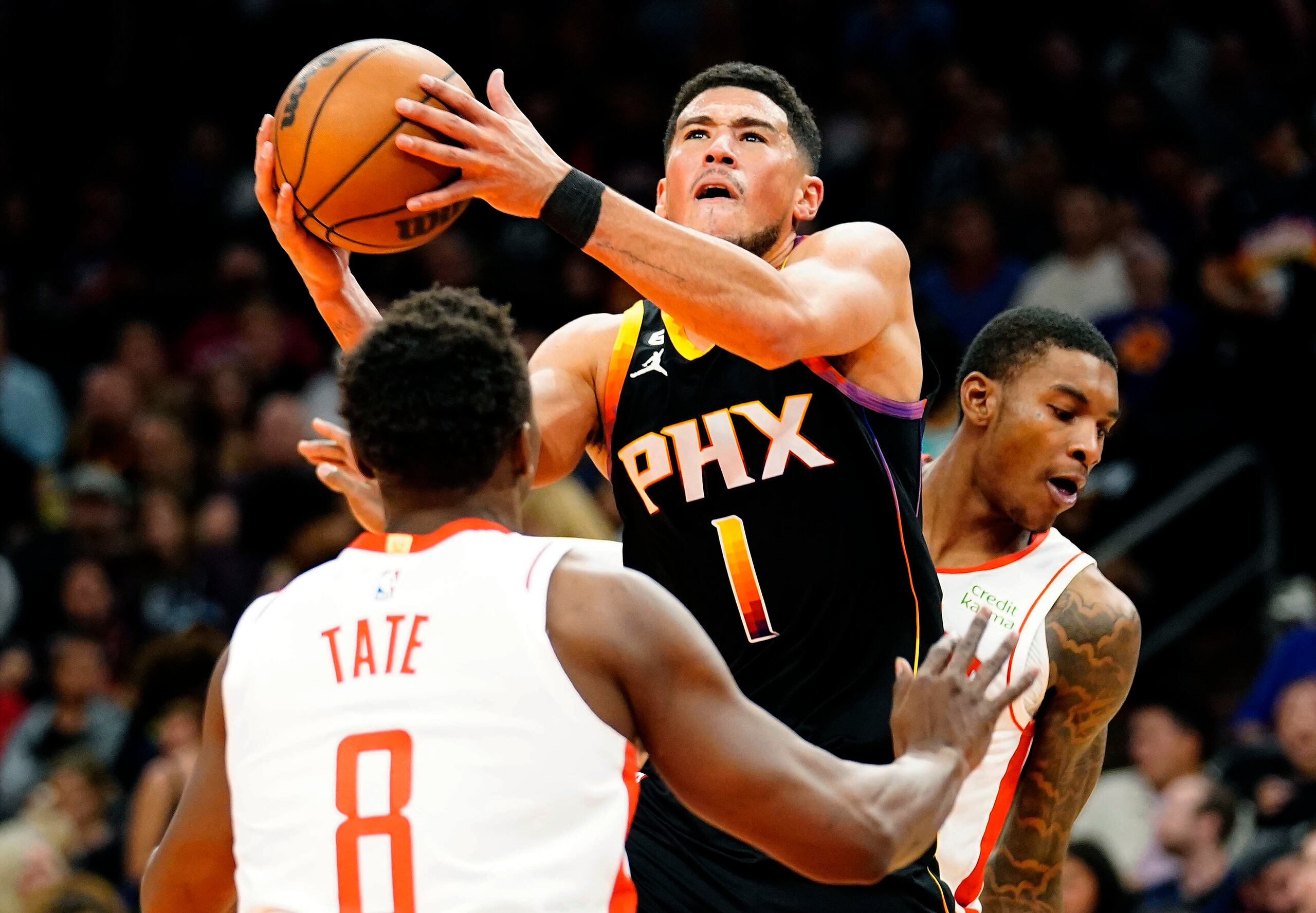 Devin Booker (1), de los Suns de Phoenix, ataca la canasta entre Jae'Sean Tate (8) y Kevin Porter Jr. (3), de los Rockets de Houston, durante la segunda mitad del juego de baloncesto de la NBA, el domingo 30 de octubre de 2022, en Phoenix. (AP Foto/Darryl Webb)