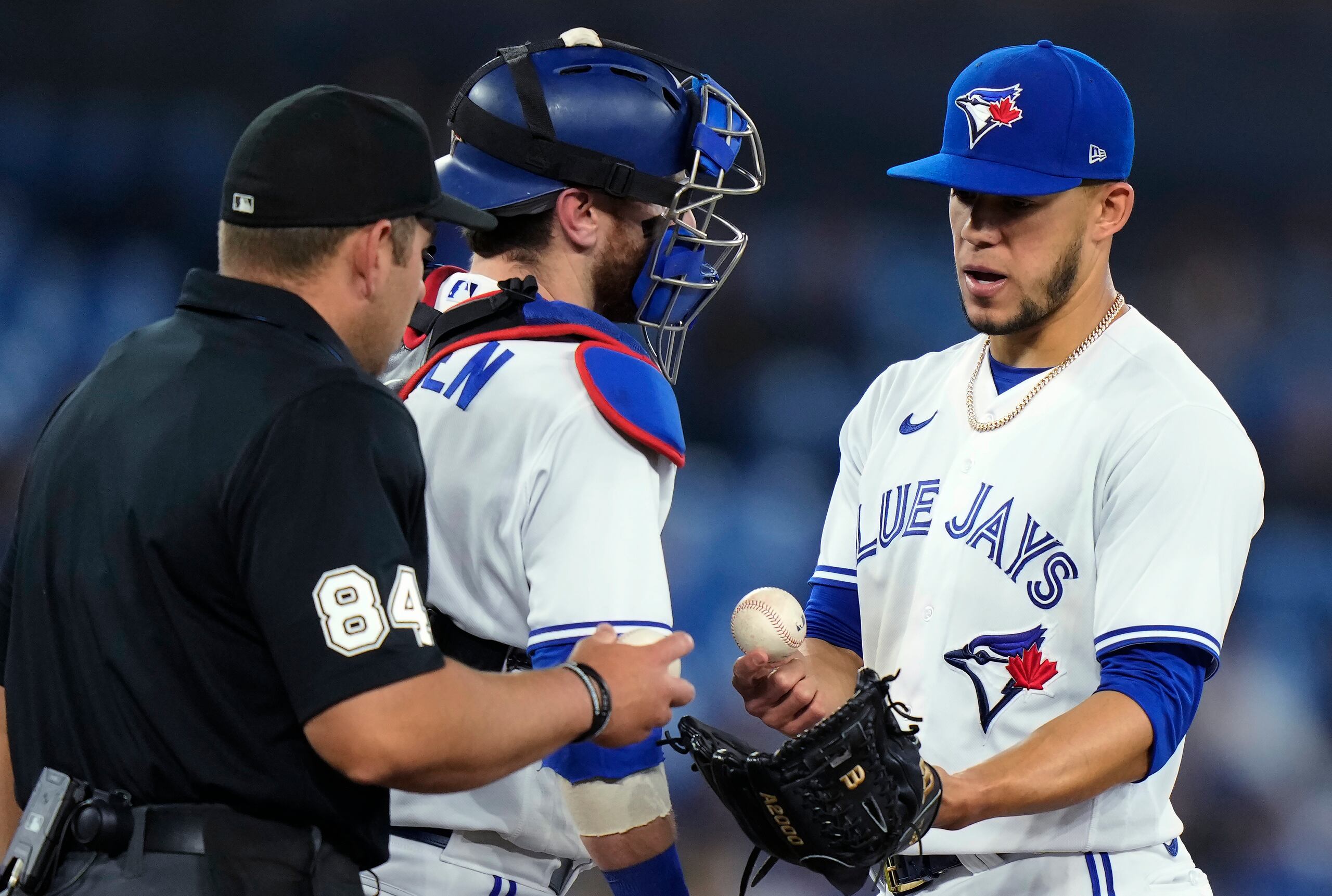 El árbitro John Libka y el receptor de los Blue Jays, Danny Jansen, visitan a José Berríos en la lomita luego de que este último fuese alcanzado por un batazo de línea de parte de Aaron Hicks en la quinta entrada del jueves.