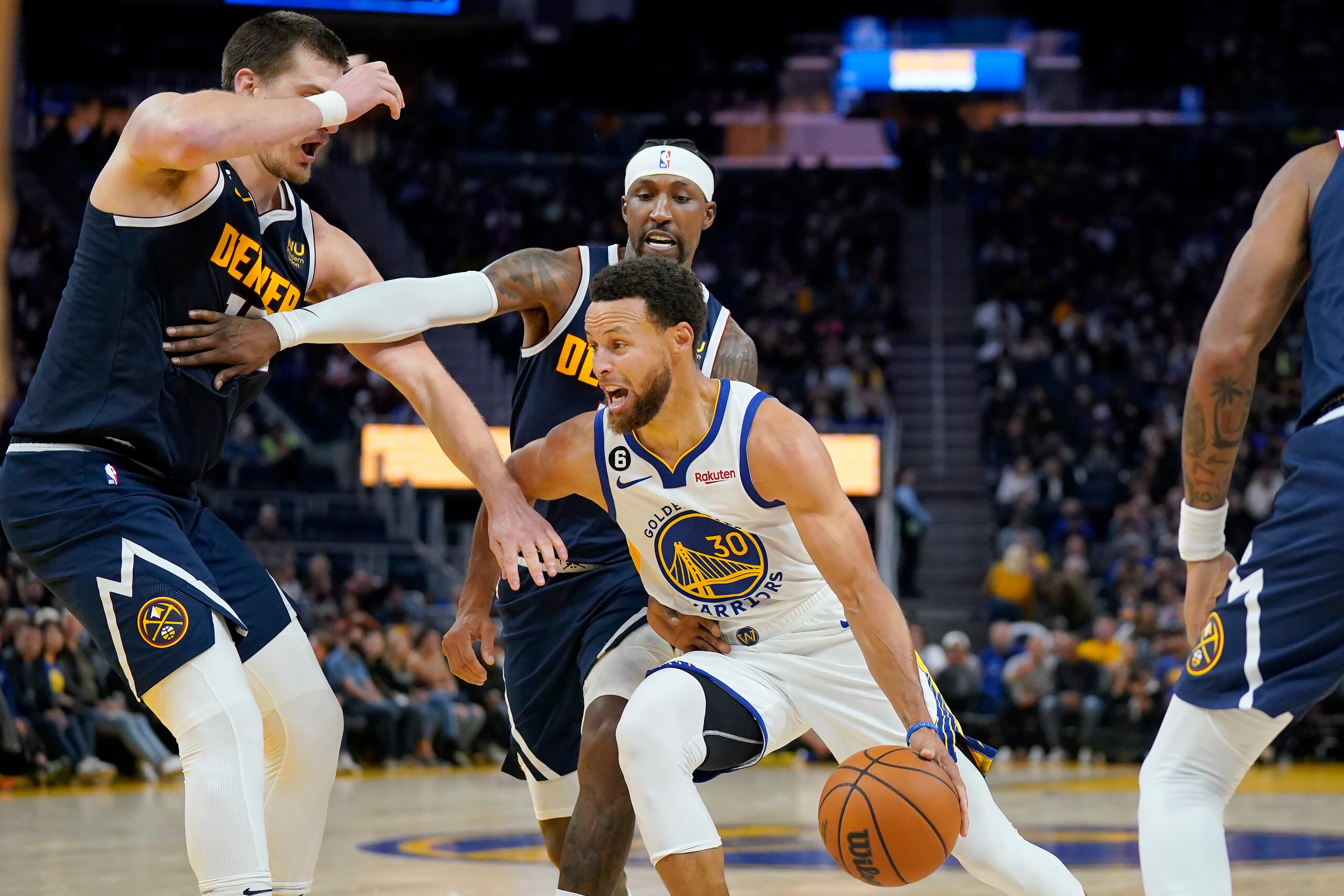 El base de los Warriors de Golden State Stephen Curry avanza hacia la canasta mientras lo defienden el pívot Nikola Jokic y el base Kentavious Caldwell-Pope de los Nuggets de Denver en el encuentro de pretemporada del viernes 14 de octubre del 2022.