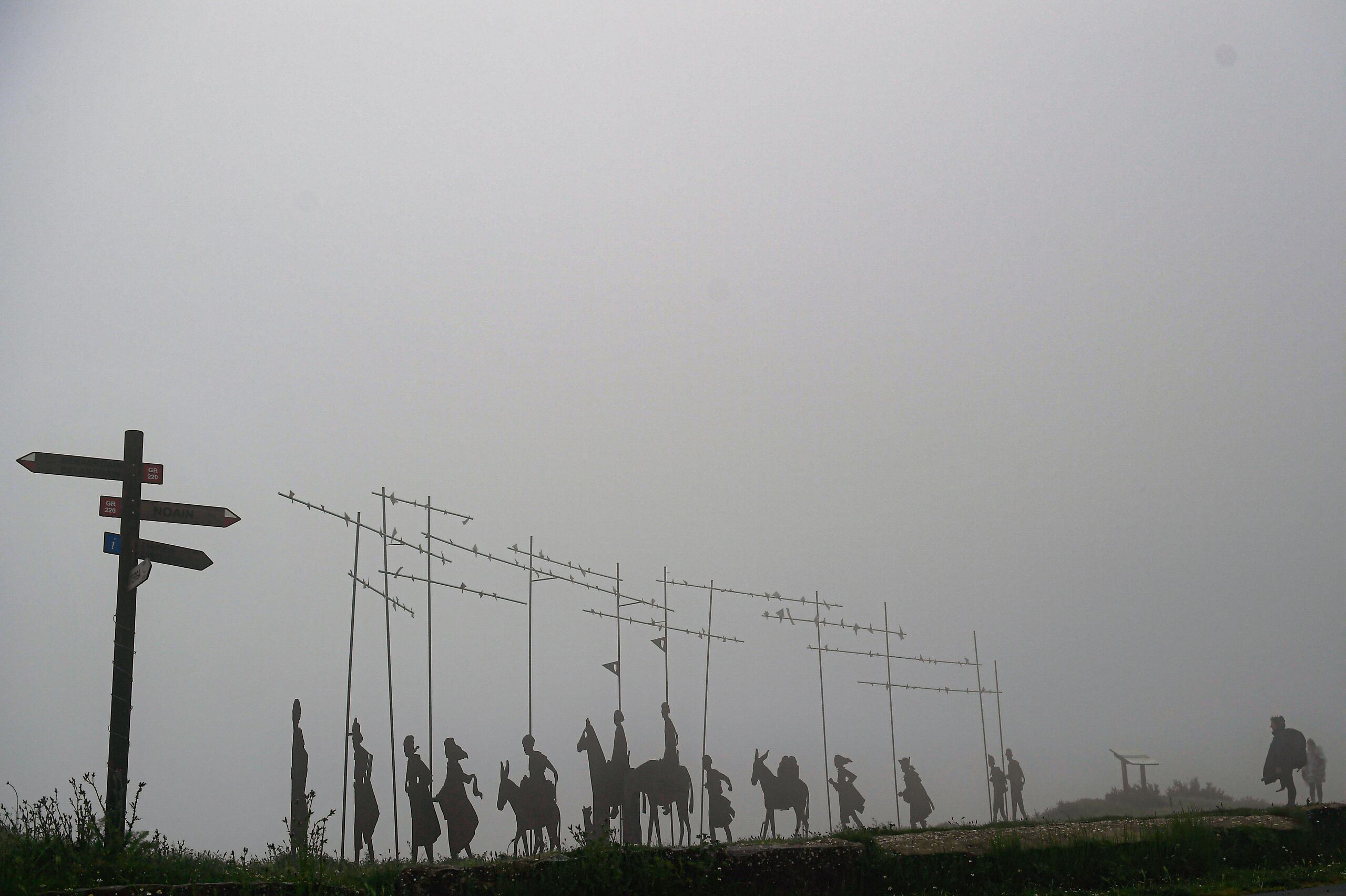 Peregrinos caminan junto a esculturas que indican la dirección del Camino de Santiago en la montaña El Perdón, cerca de Pamplona, España.