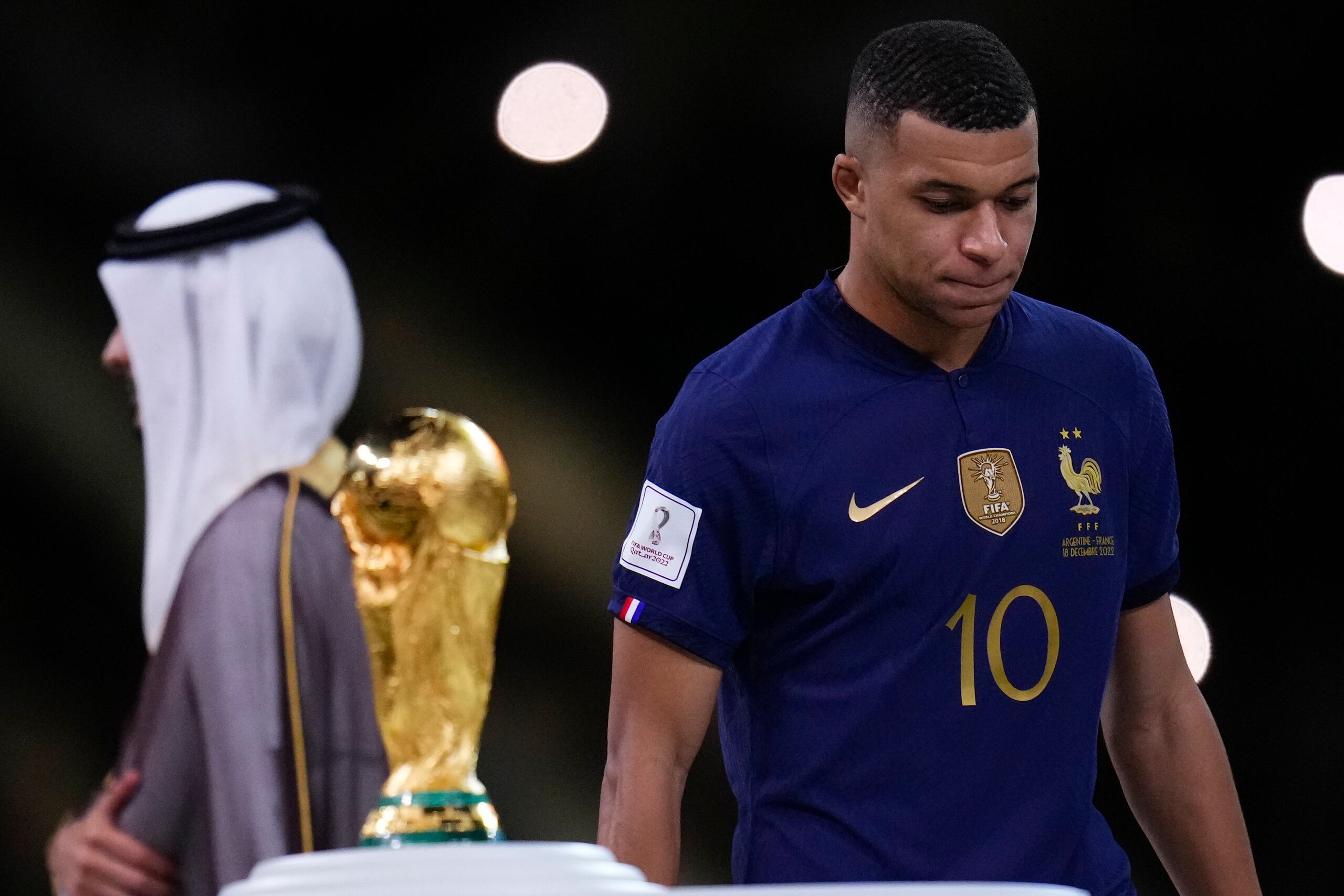 Kylian Mbappe pasa cabizbajo al lado del trofeo de la Copa Mundial tras perder ante Argentina.