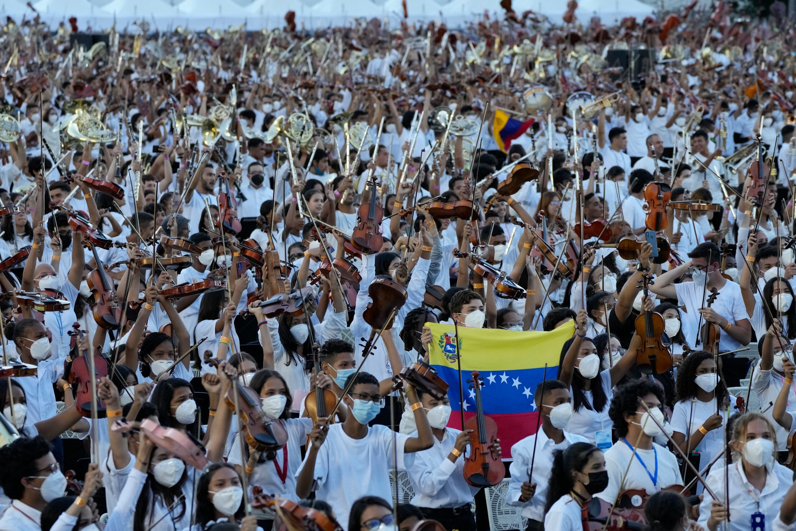 Miembros del Sistema Nacional de Orquestas levantan sus instrumentos y agitan banderas venezolanas al terminar de tocar una pieza de 12 minutos, la "Marcha Eslava", de Tchaikovski, en un intento para romper la marca del Guinness World Record del manyor número de instrumentos utilizados, en Caracas, Venezuela, el sábado 13 de noviembre de 2021. (AP Photo/Ariana Cubillos)