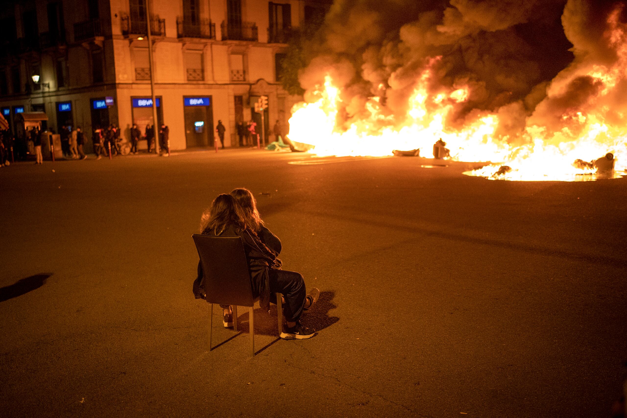 Dos mujeres sentadas contemplan una barricada en llamas erigida por manifestantes durante una protesta contra el arresto del rapero Pablo Hasél, en Barcelona, España.