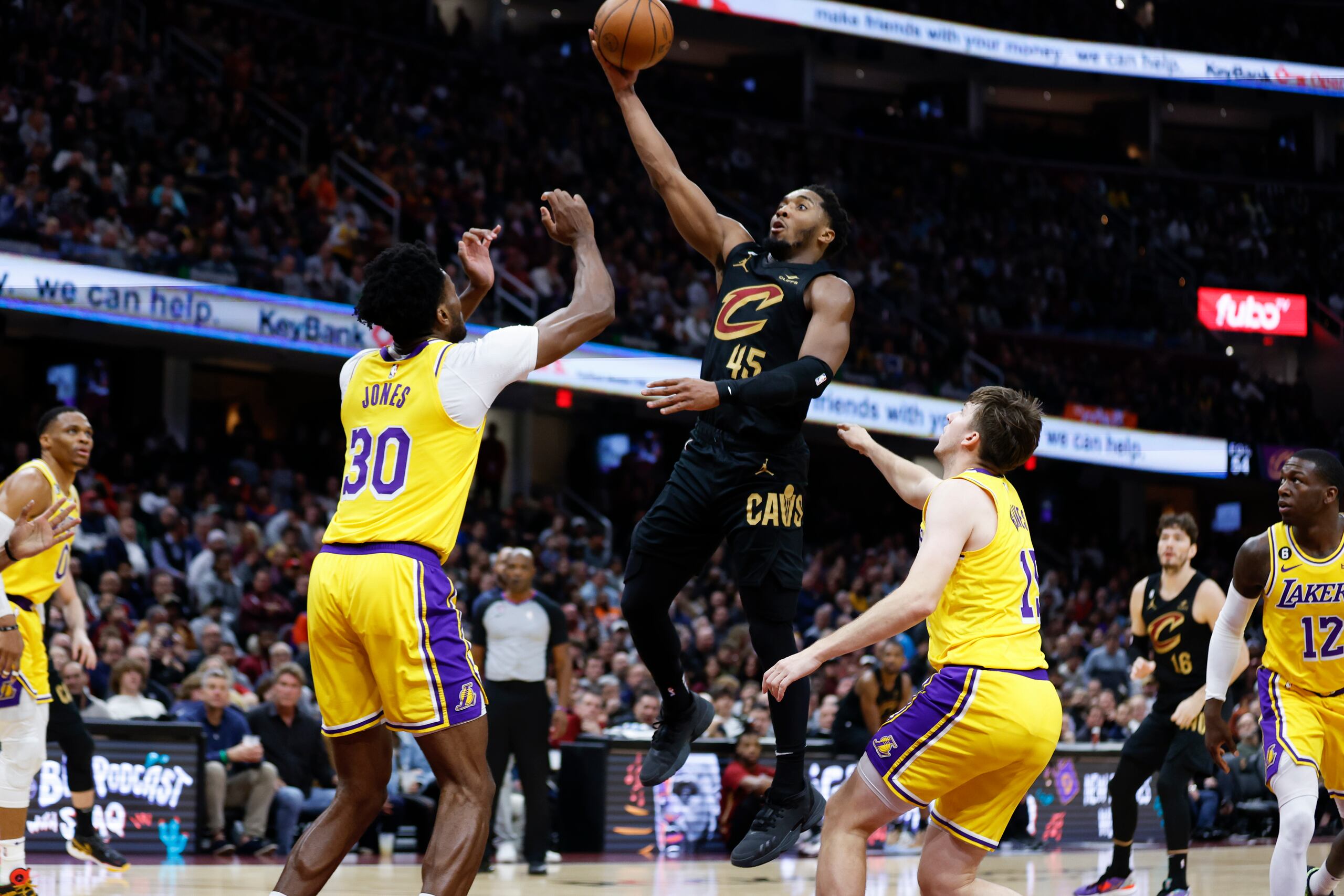 El armador de los Cavaliers de Cleveland, se levanta rumbo al canasto ante el centro de los Lakers de Los Ángeles, Damian Jones, y el base Austin Reaves.