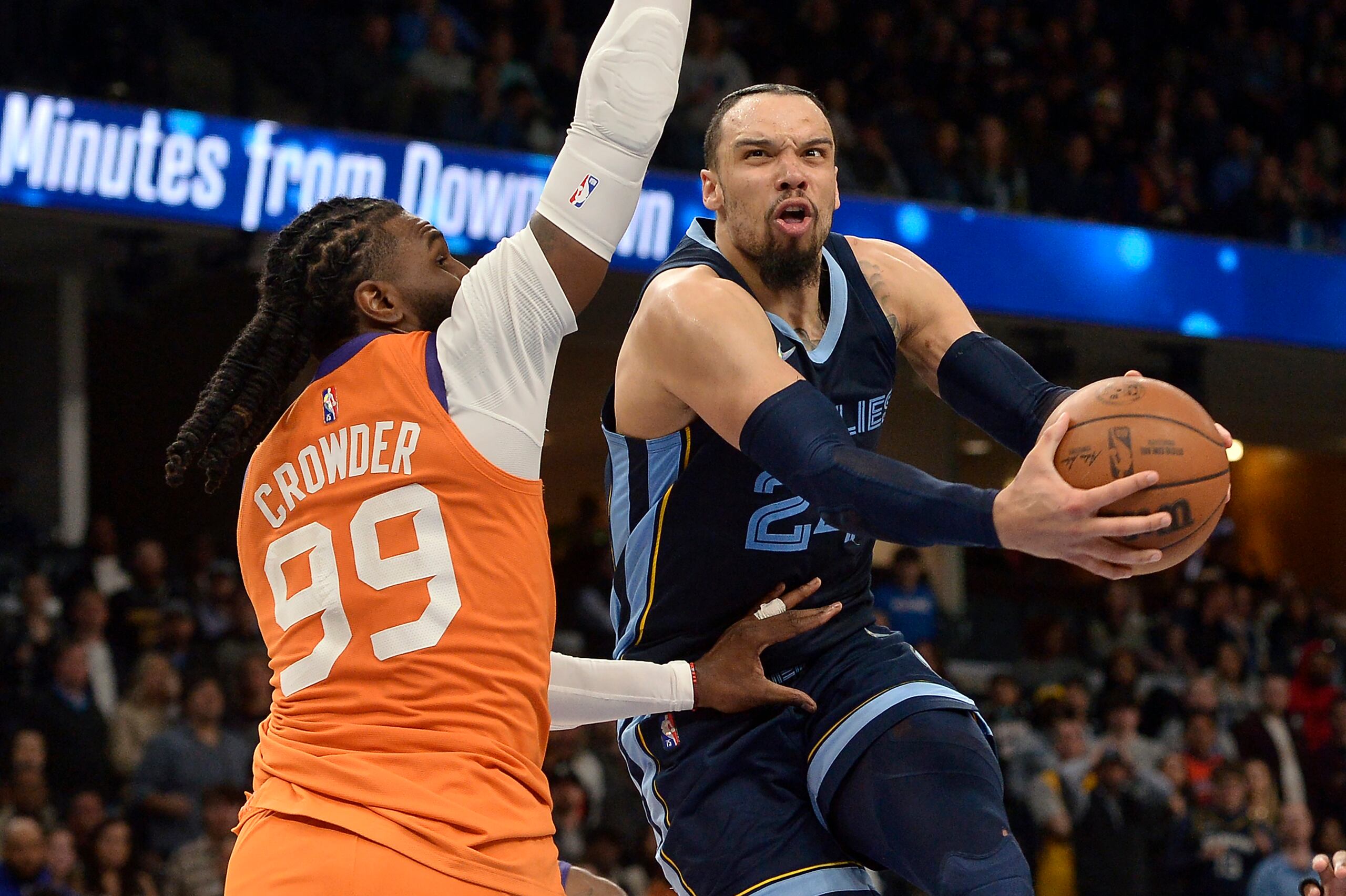 Dillon Brooks, de los Grizzlies de Memphis, con el balón, se contorsiona para realizar un intento frente a la defensa de Jae Crowder (99), de los SUns de Phoenix.