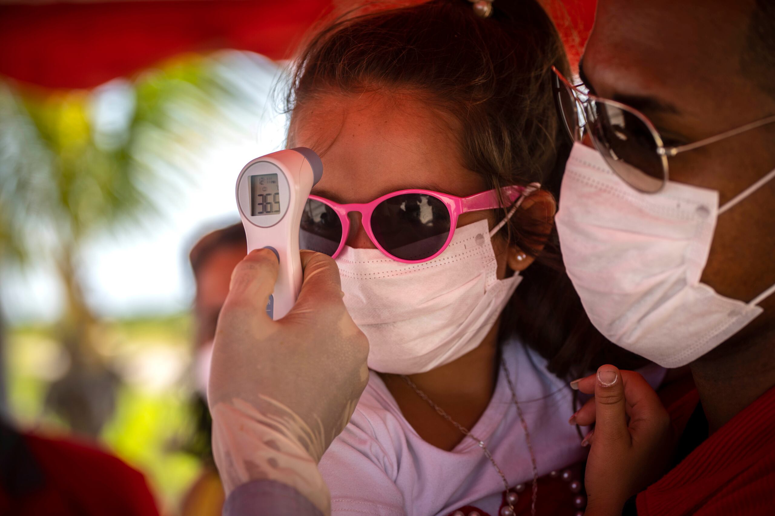 A una niña con mascarilla para protegerse del nuevo coronavirus le toman la temperatura en un puesto de control policial en la entrada de la provincia de La Habana, Cuba