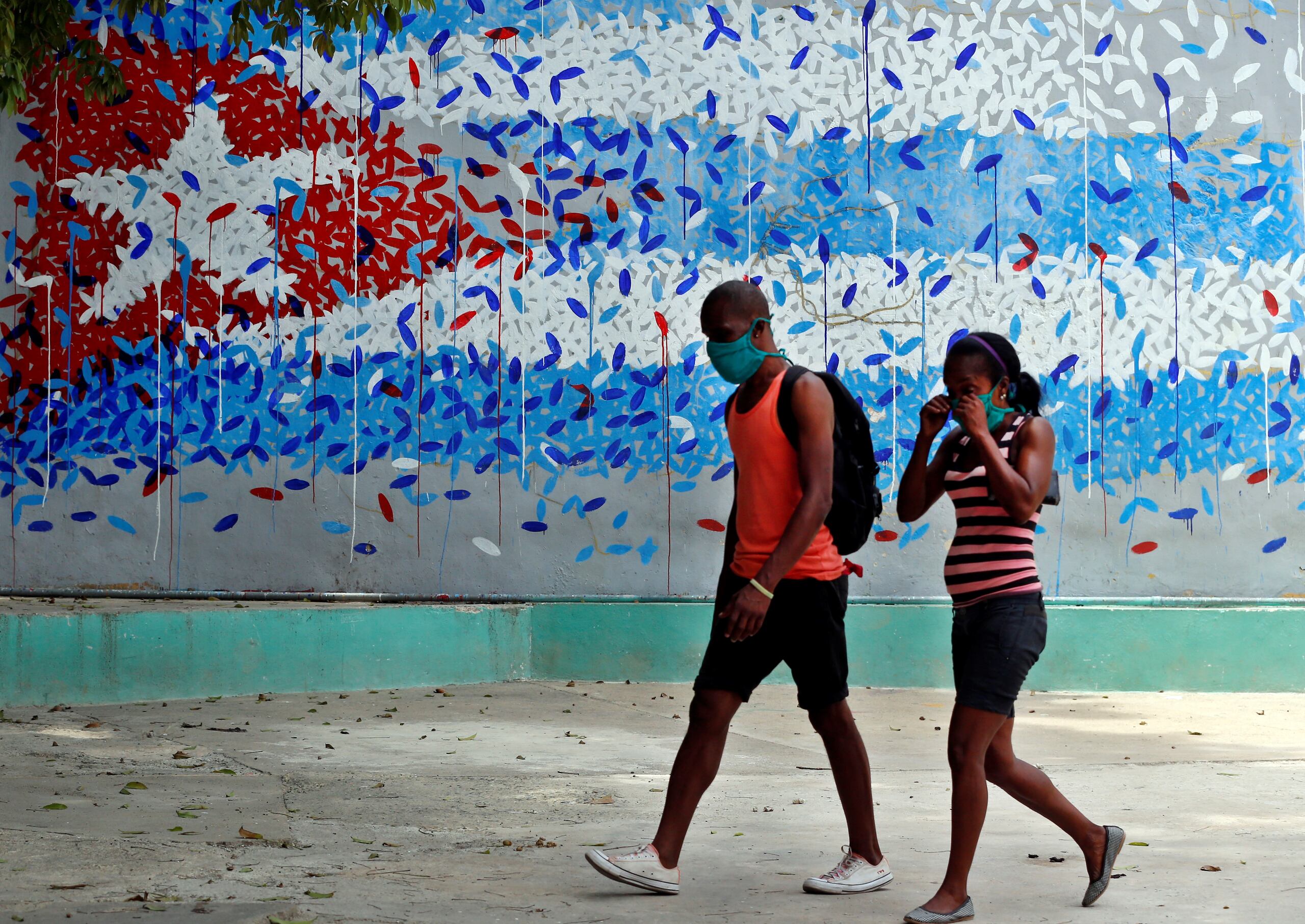 Una pareja con tapabocas camina junto a un graffitis con la imagen de la bandera cubana, en La Habana (Cuba).