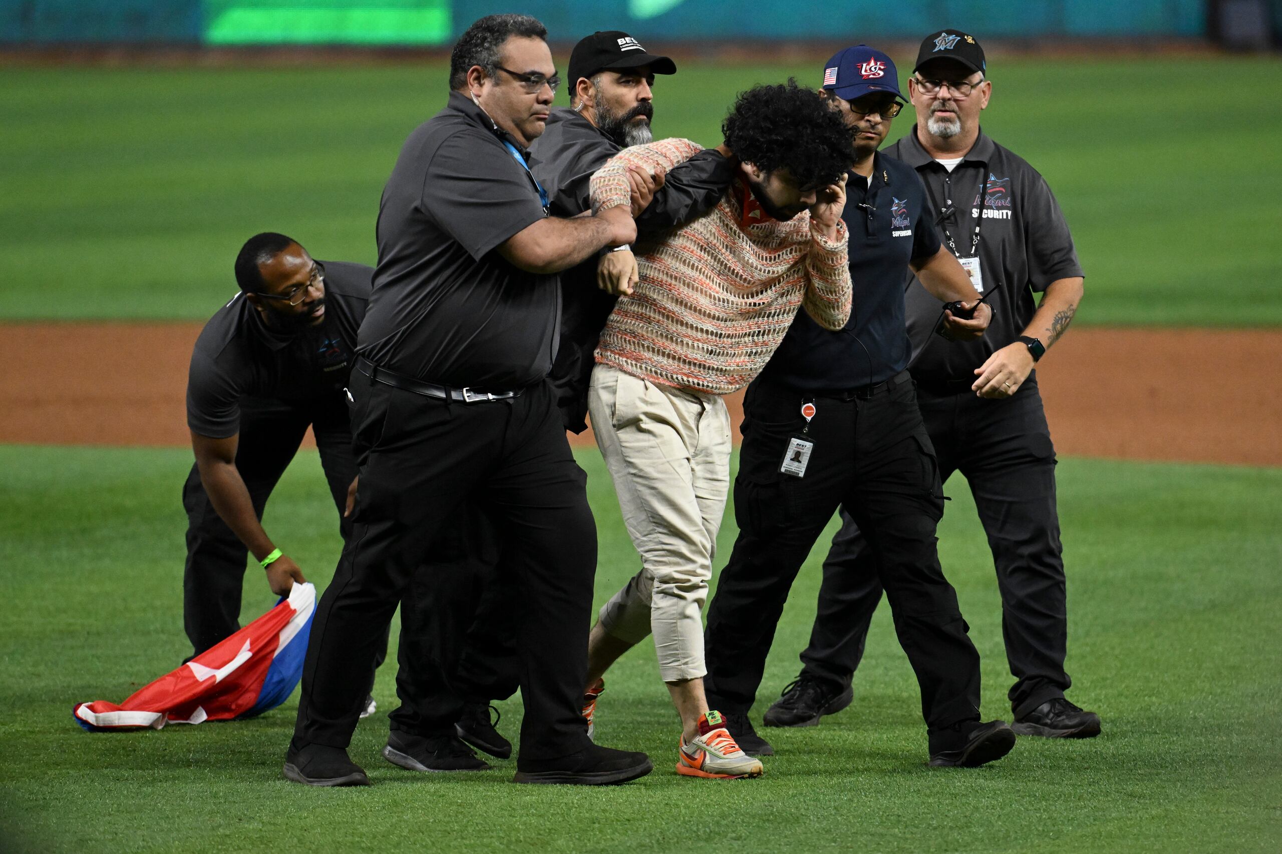 El joven que entró al terreno con una bandera de Cuba es retirado del área por agentes de seguridad del estadio.