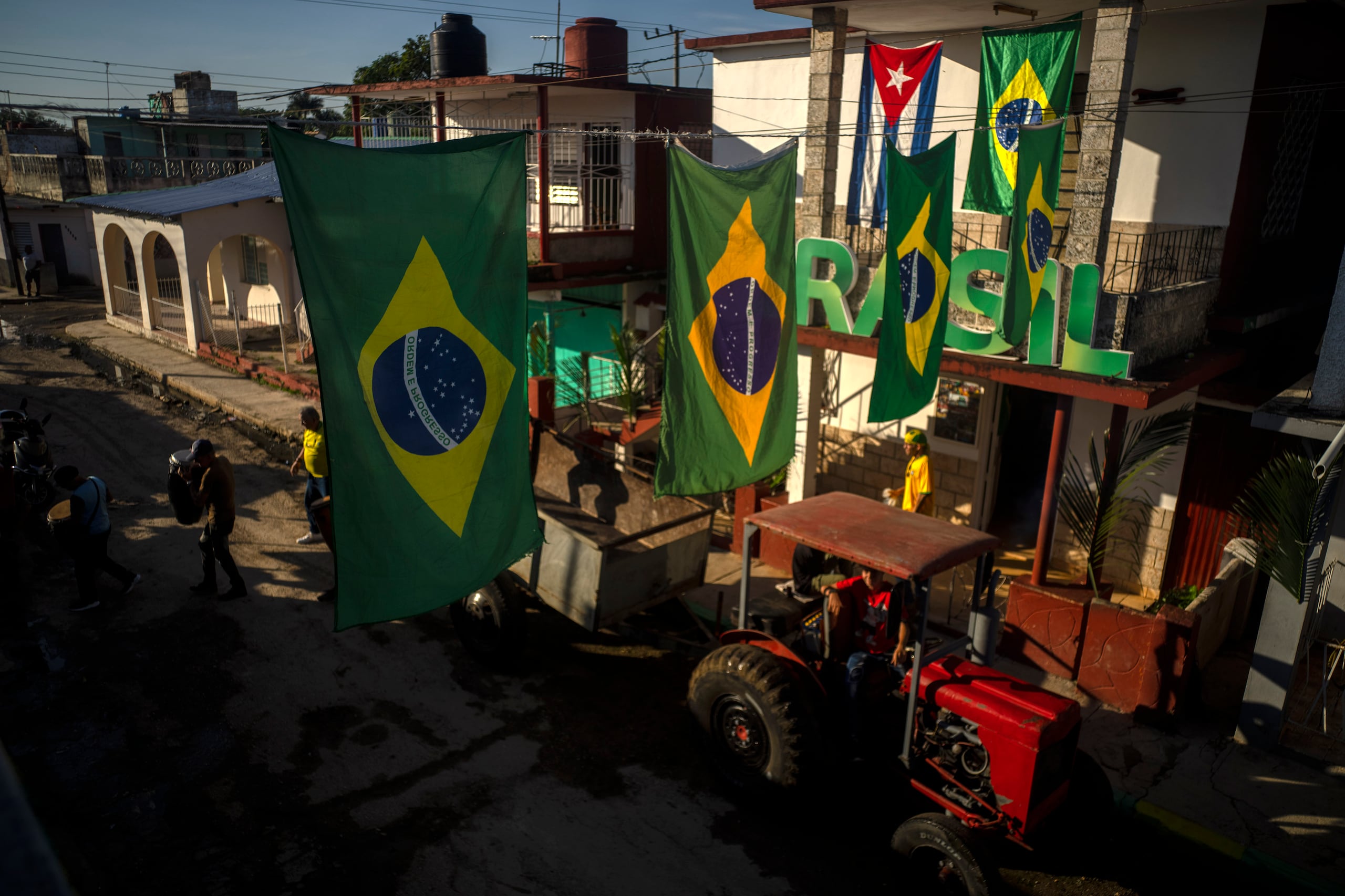 Banderas de Brasil cuelgan por encima de un tractor que transportó a un remolque lleno de aficionados y músicos a casa del presidente de una asociación de seguidores de la selección brasileña en Bauta, Cuba, el lunes 28 de noviembre de 2022 (AP Photo/Ramón Espinosa)