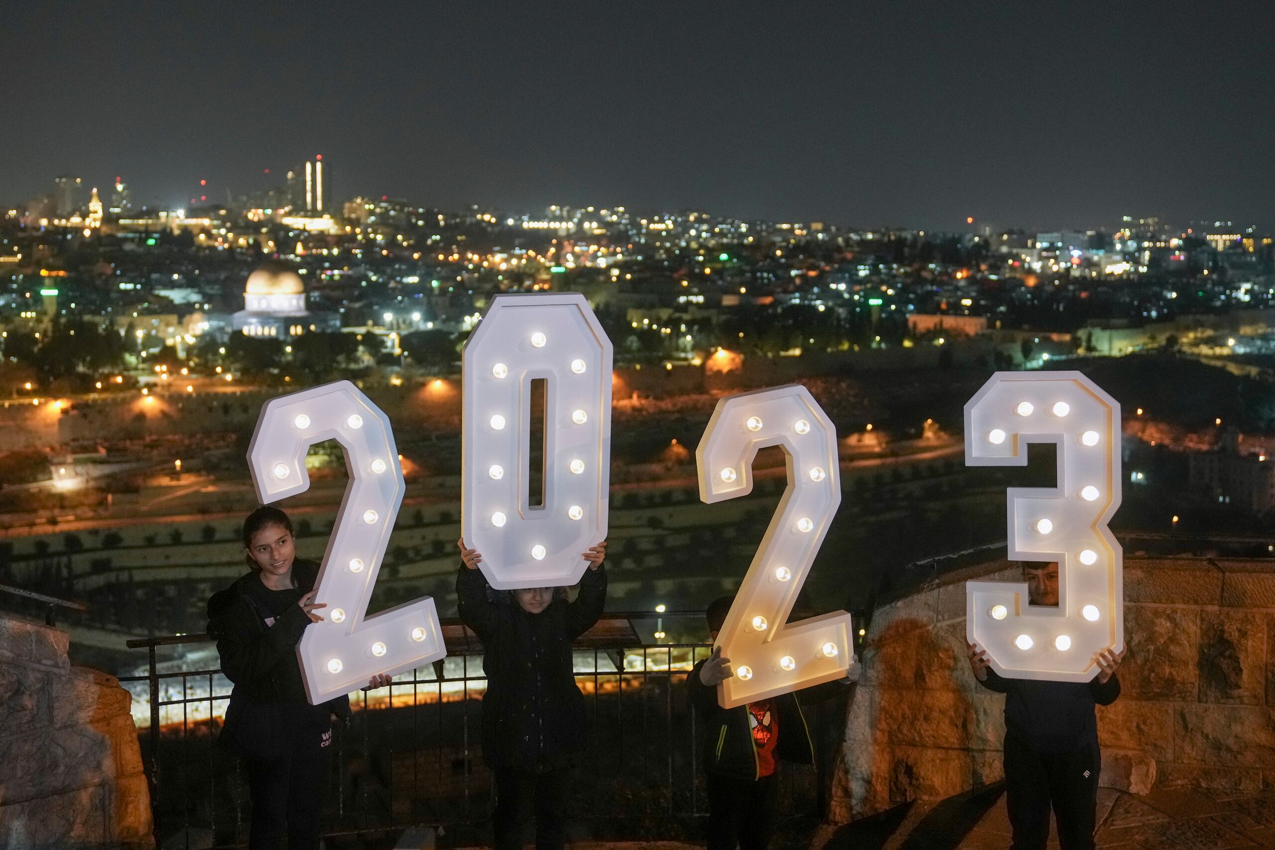 Personas forman con números 2023 mientras celebran la víspera del Año Nuevo en el Monte de los Olivos frente a la Ciudad Antigua de Jerusalén, Israel.