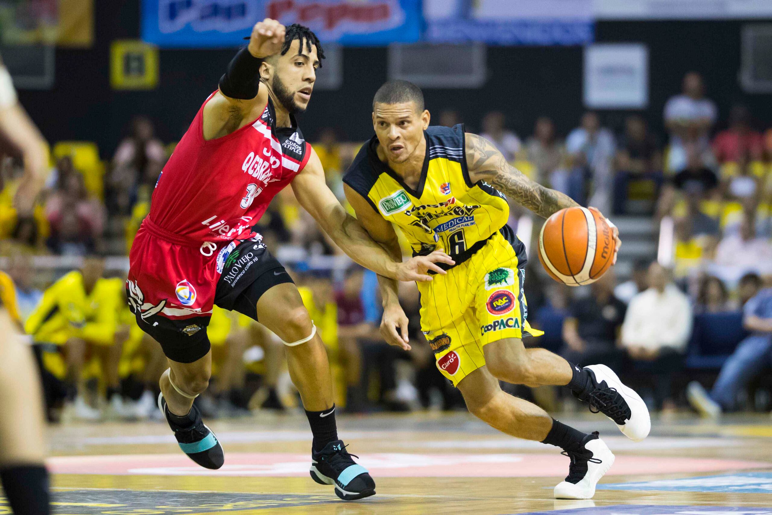 Denis Clemente, de los Capitanes, maneja el balón contra Jorge L. Matos, de los Piratas.