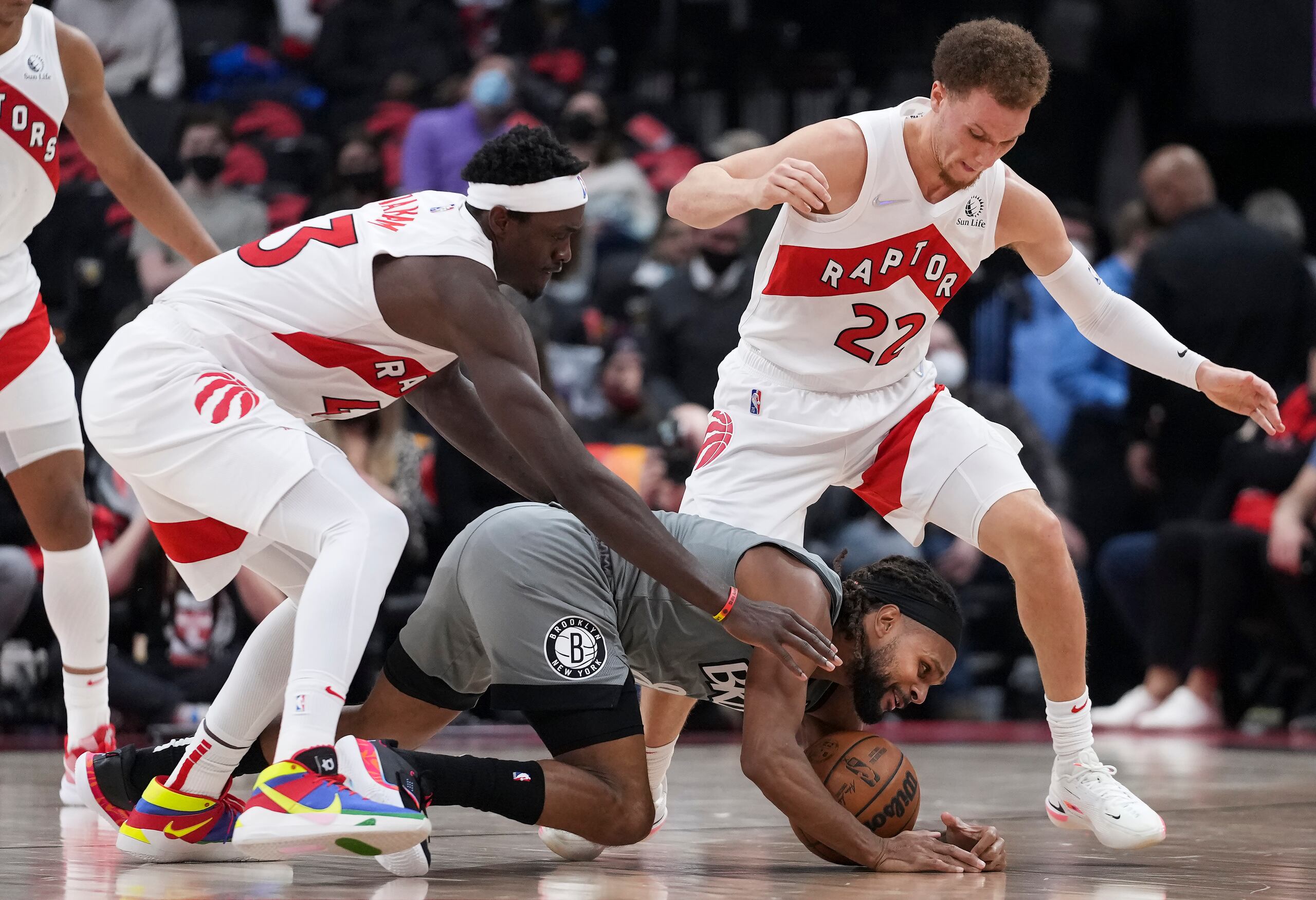 Patty Mills, de los Nets de Brooklyn, al centro, intenta retener el balón luego de quedar atrapado entre la defensa de Pascal Siakam, a la izquierda, y Malachi Flynn, de los Raptors de Toronto.