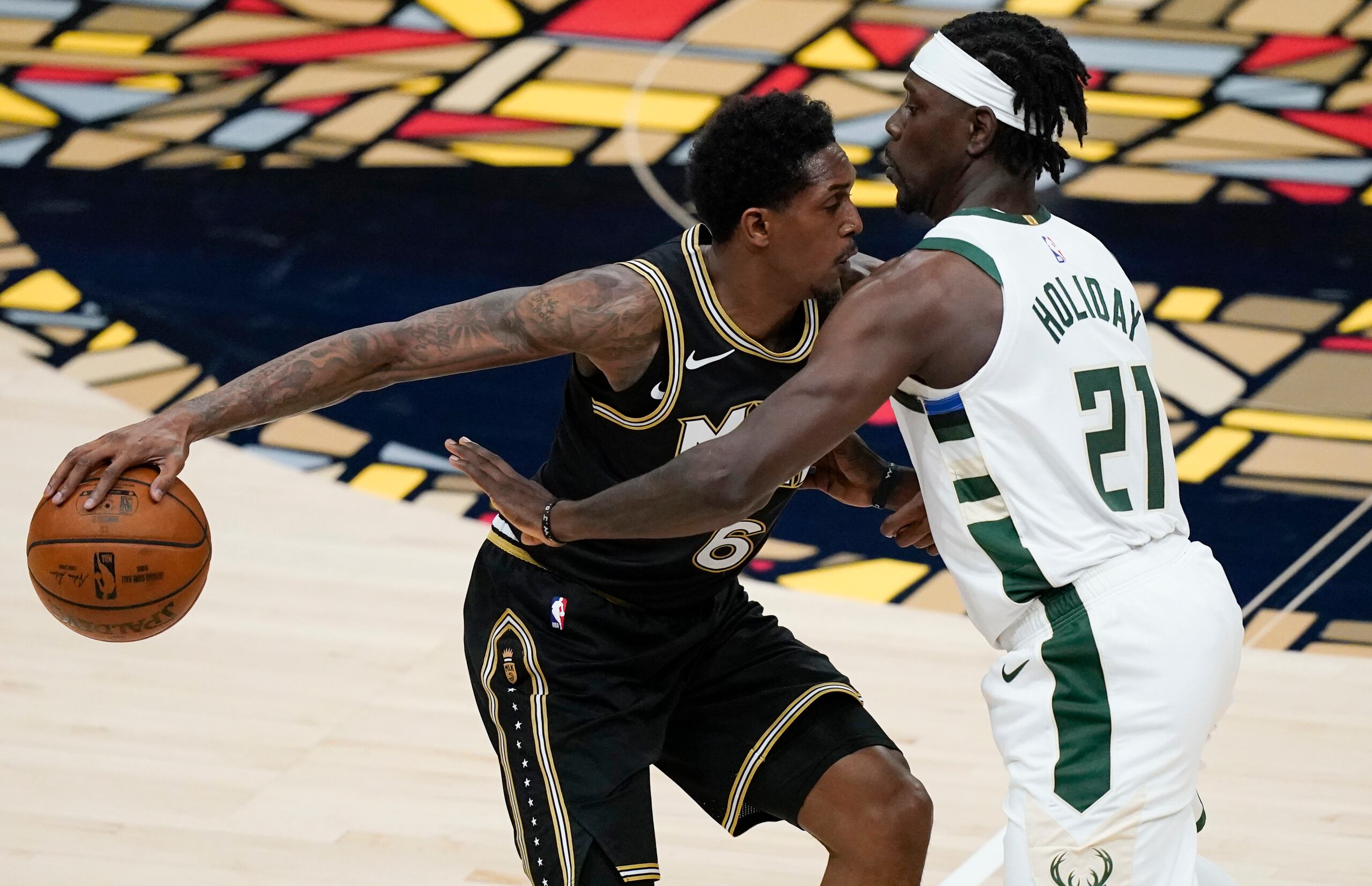 Lou Williams, de los Hawks de Atlanta, protege el balón del acoso defensivo de Jrue Holiday, de los Bucks de Milwaukee, durante el desafío del martes.