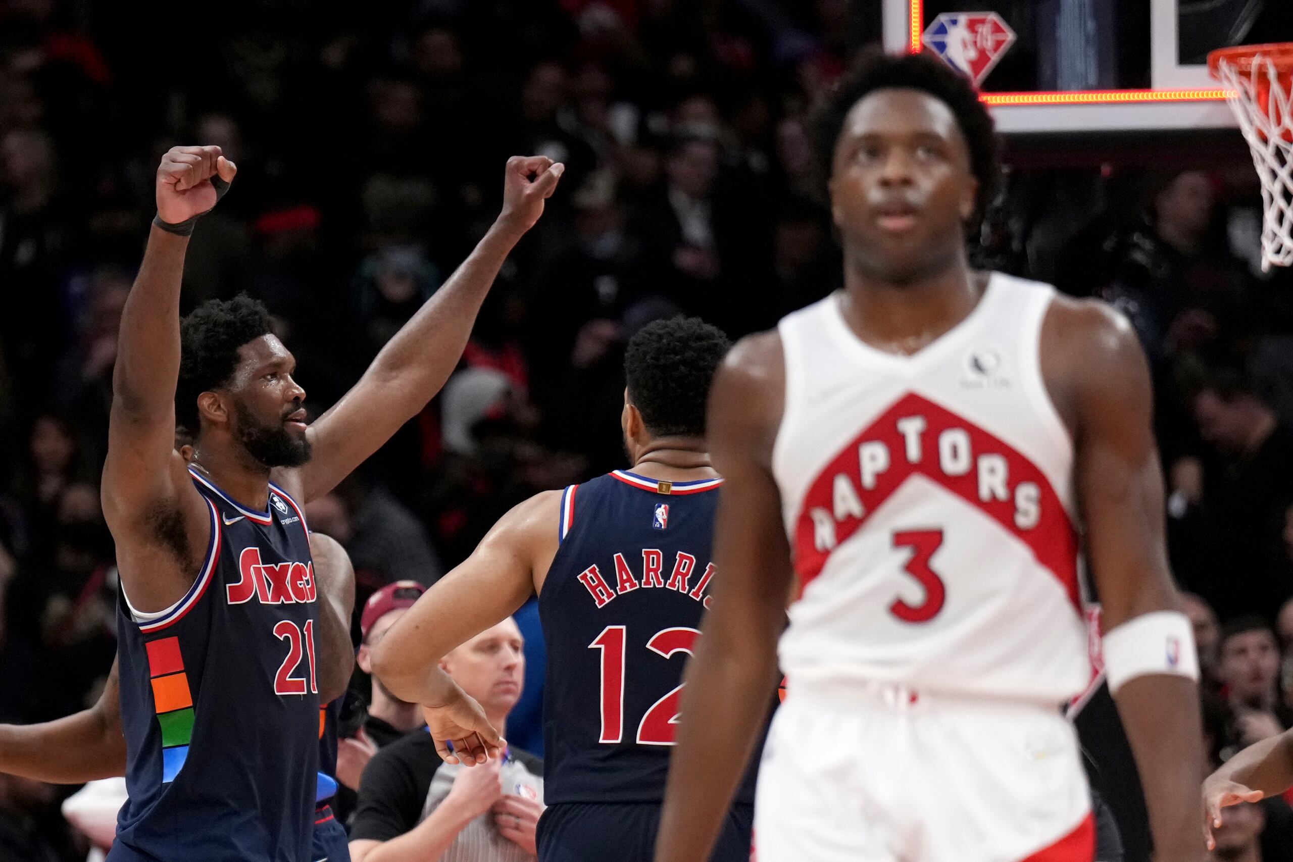 El delantero de los Raptors de Toronto, OG Anunoby (3), se retira decepcionado luego de que Joel Embiid, de los Sixers, al fondo con las manos en alto, colara un triple en el segundo final del tiempo extra que le dio la victoria a los Sixers.