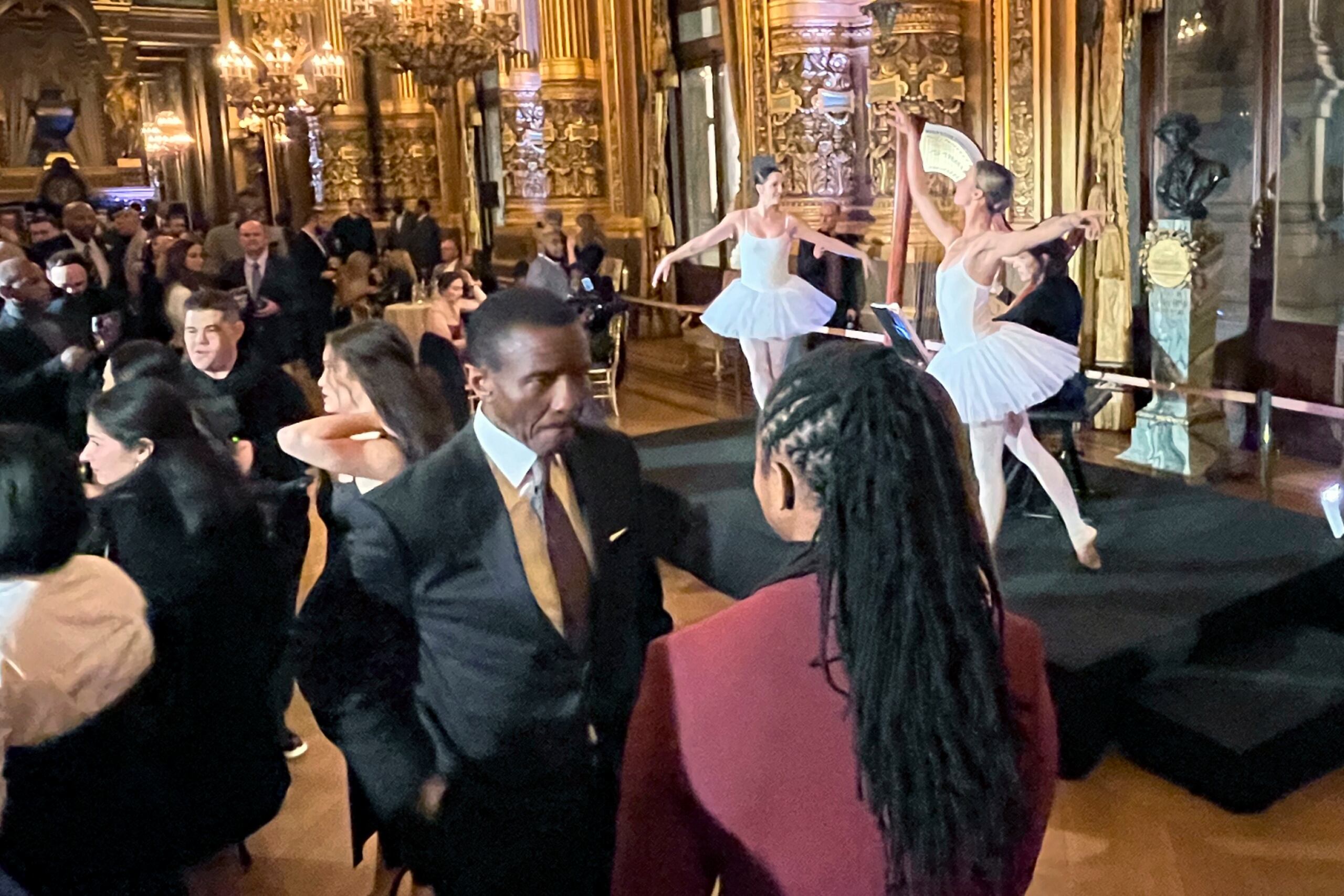 Dwayne Casey, entrenador de los Pistons, sostiene una conversación mientras al fondo hay un ballet exponiendo una danza.