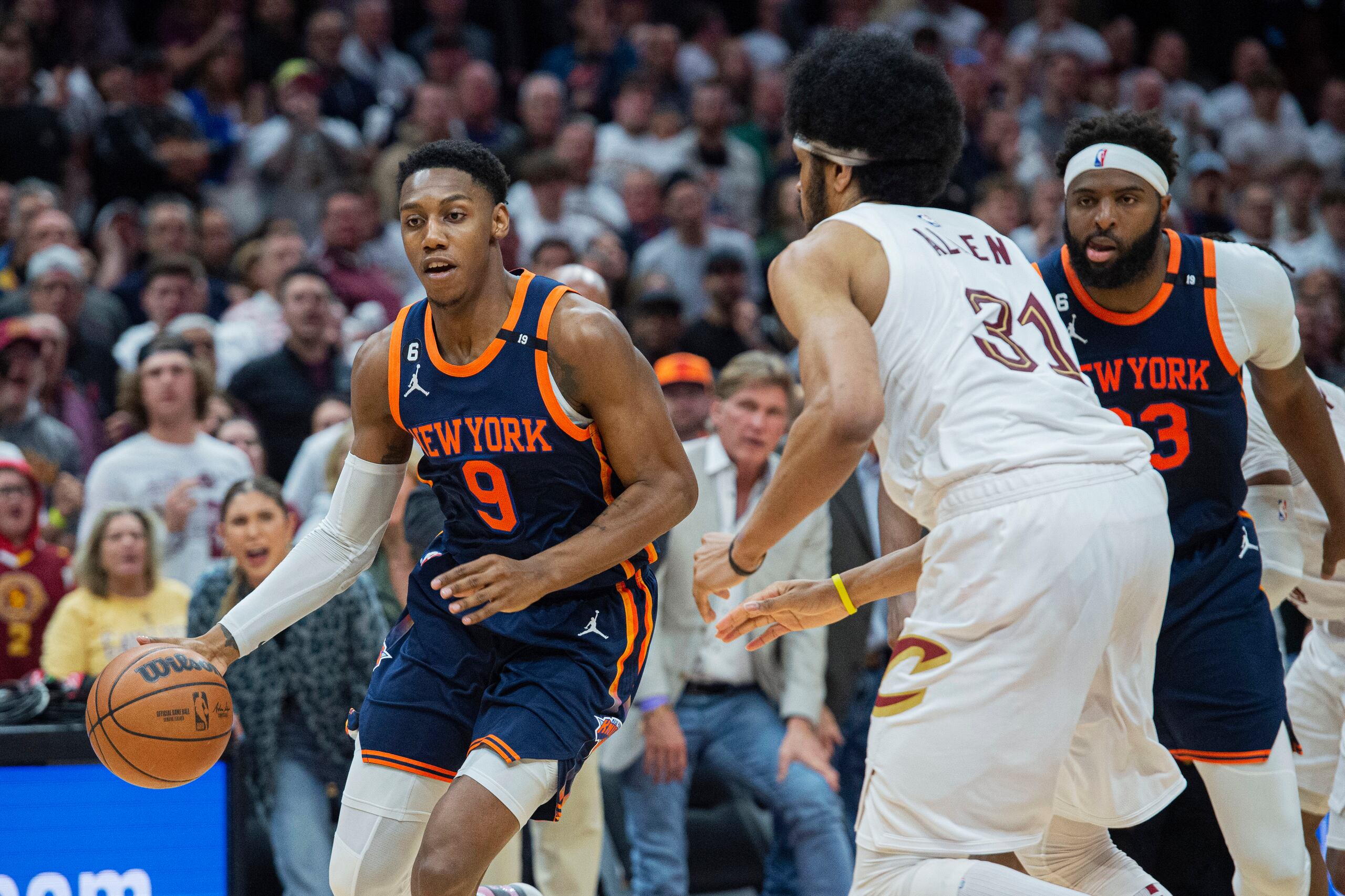 RJ Barrett (9), de los Knicks de Nueva York, conduce el balón frente a Jarrett Allen (31), de los Cavaliers de Cleveland, mientras Mitchell Robinson (23), de Nueva York, le observa.