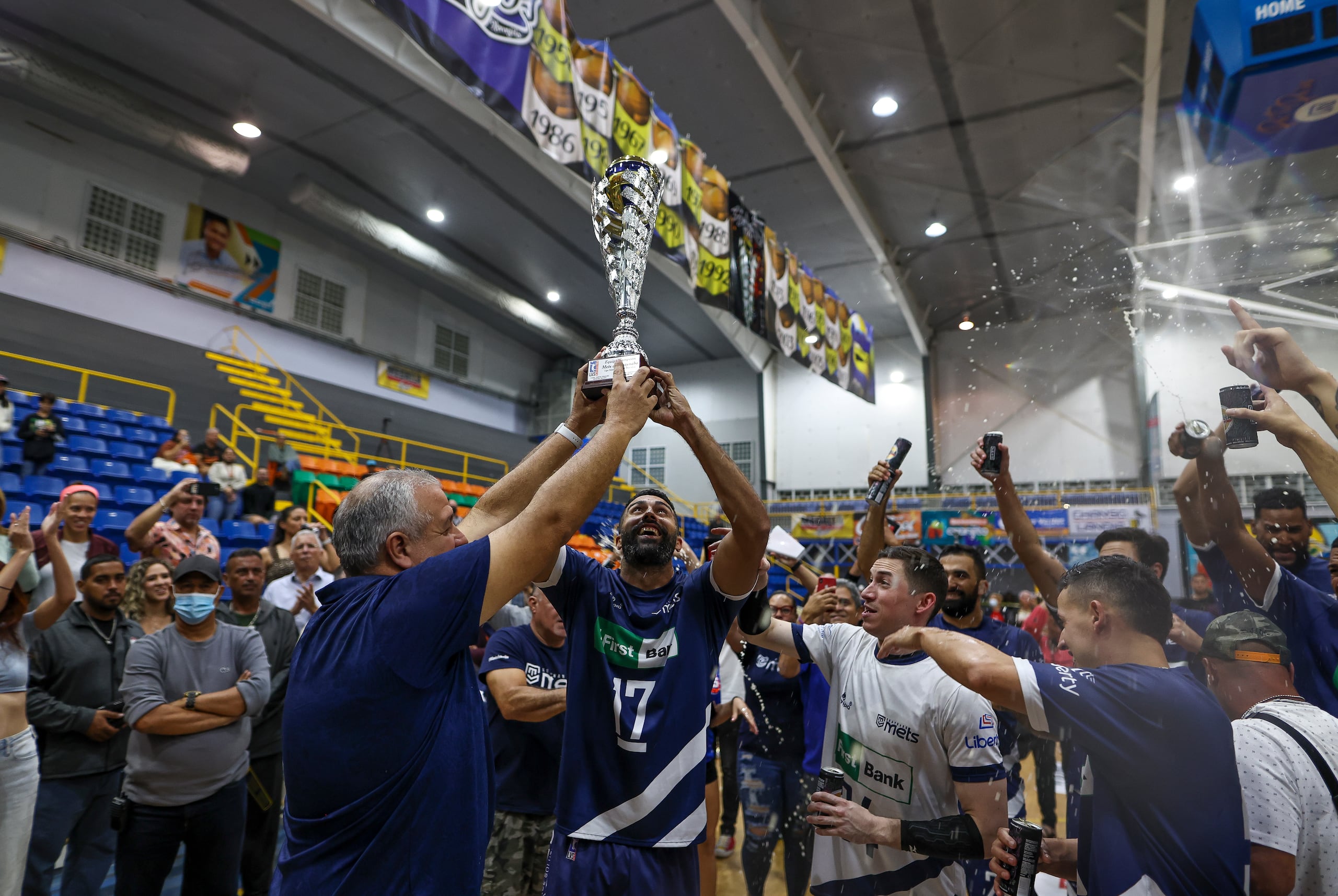 El coapoderado de los Mets, Hugo Pérez, y el opuesto Jean Carlos Ortiz levantan el trofeo de campeones del Voleibol Superior 2022.