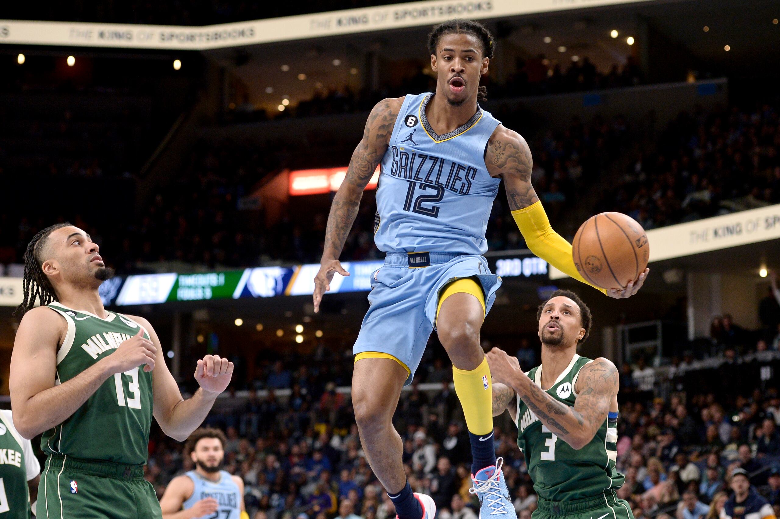 Ja Morant, de los Grizzlies de Memphis, maneja el balón en el aire mientras penetra entre la defensa de los Bucks de Milwaukee.