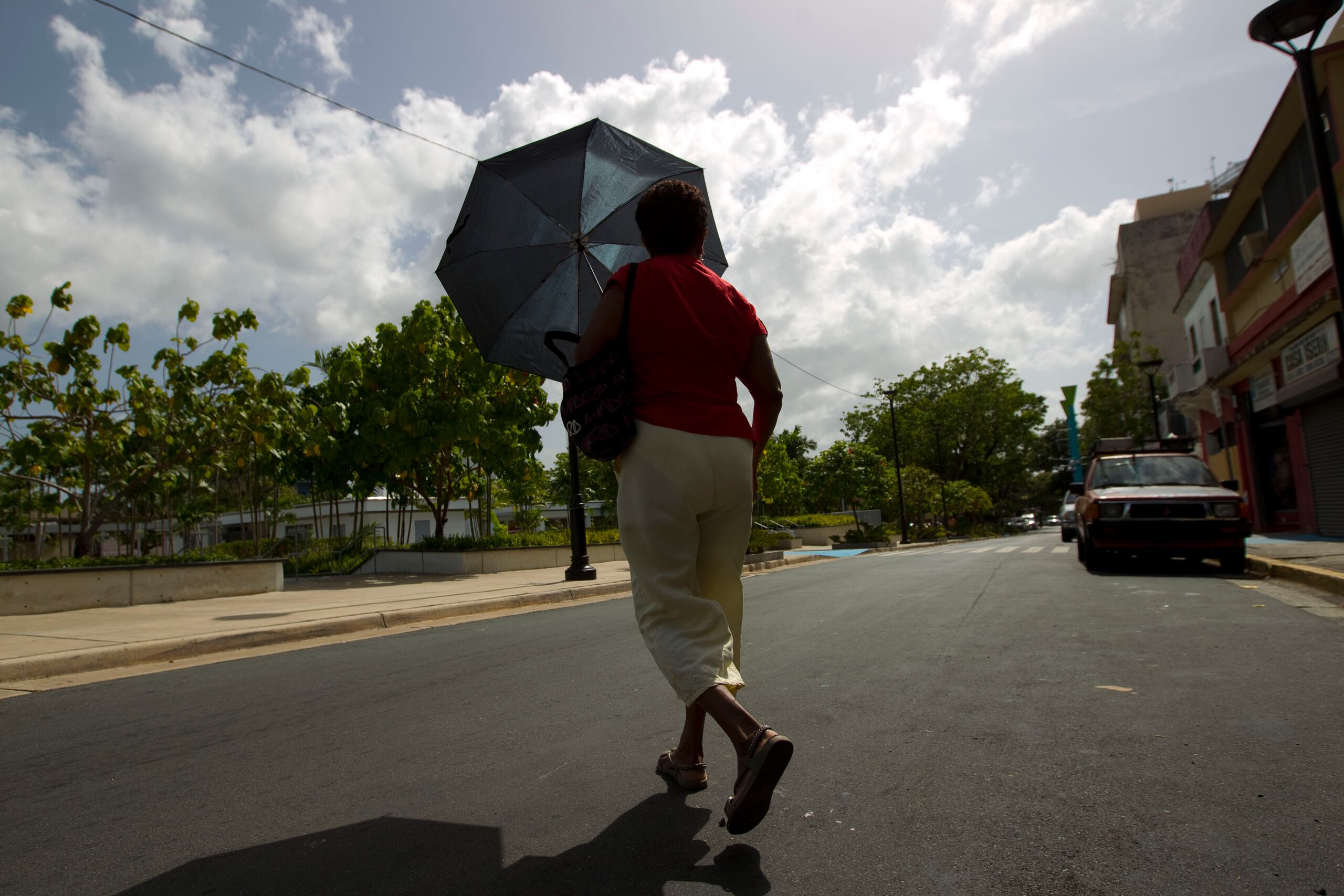 Una mujer camina con una sombrilla para cubrirse de sol.