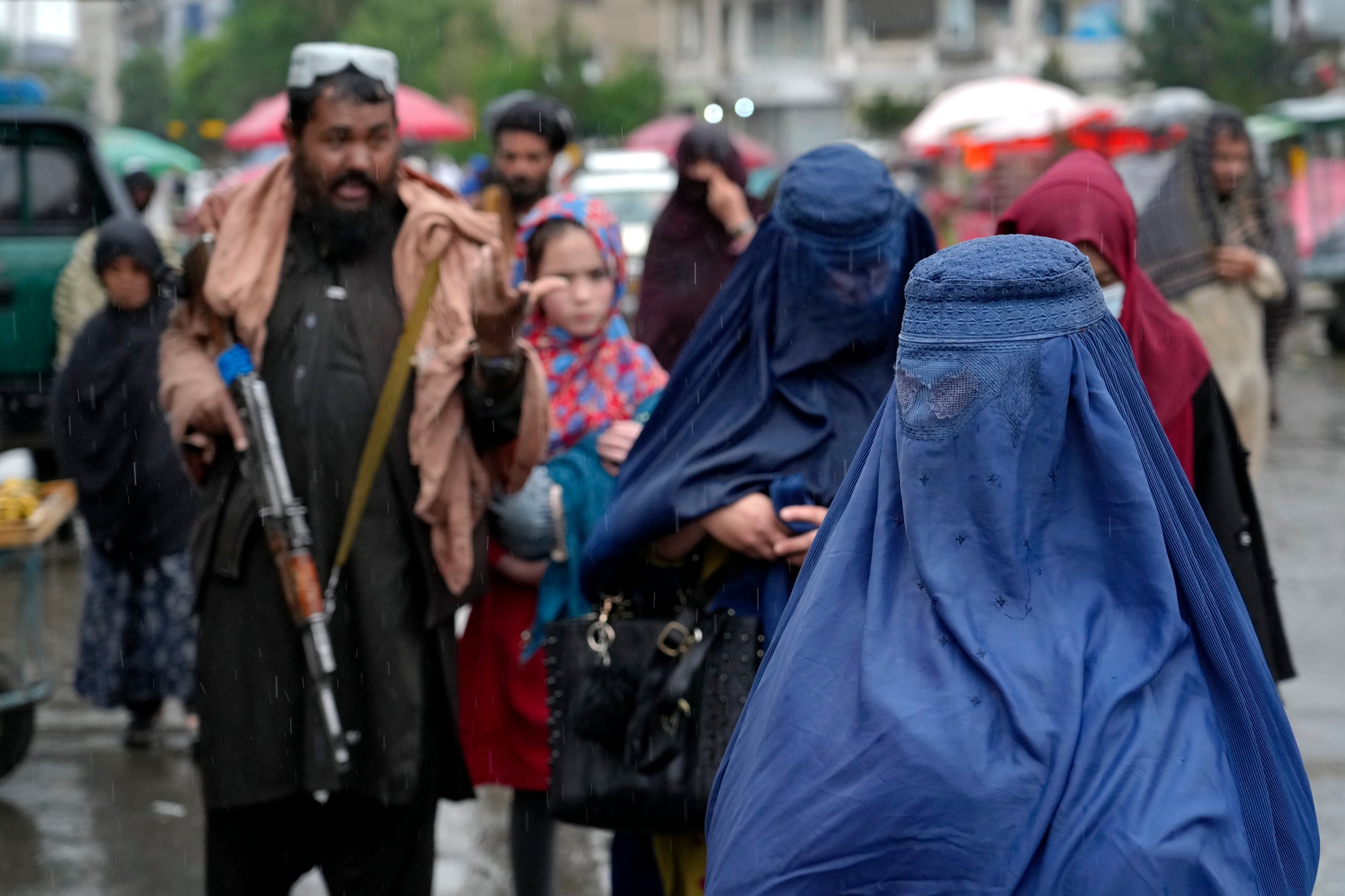 Mujeres afganas atraviesan un mercado mientras un guardia talibán vigila en el centro de Kabul.