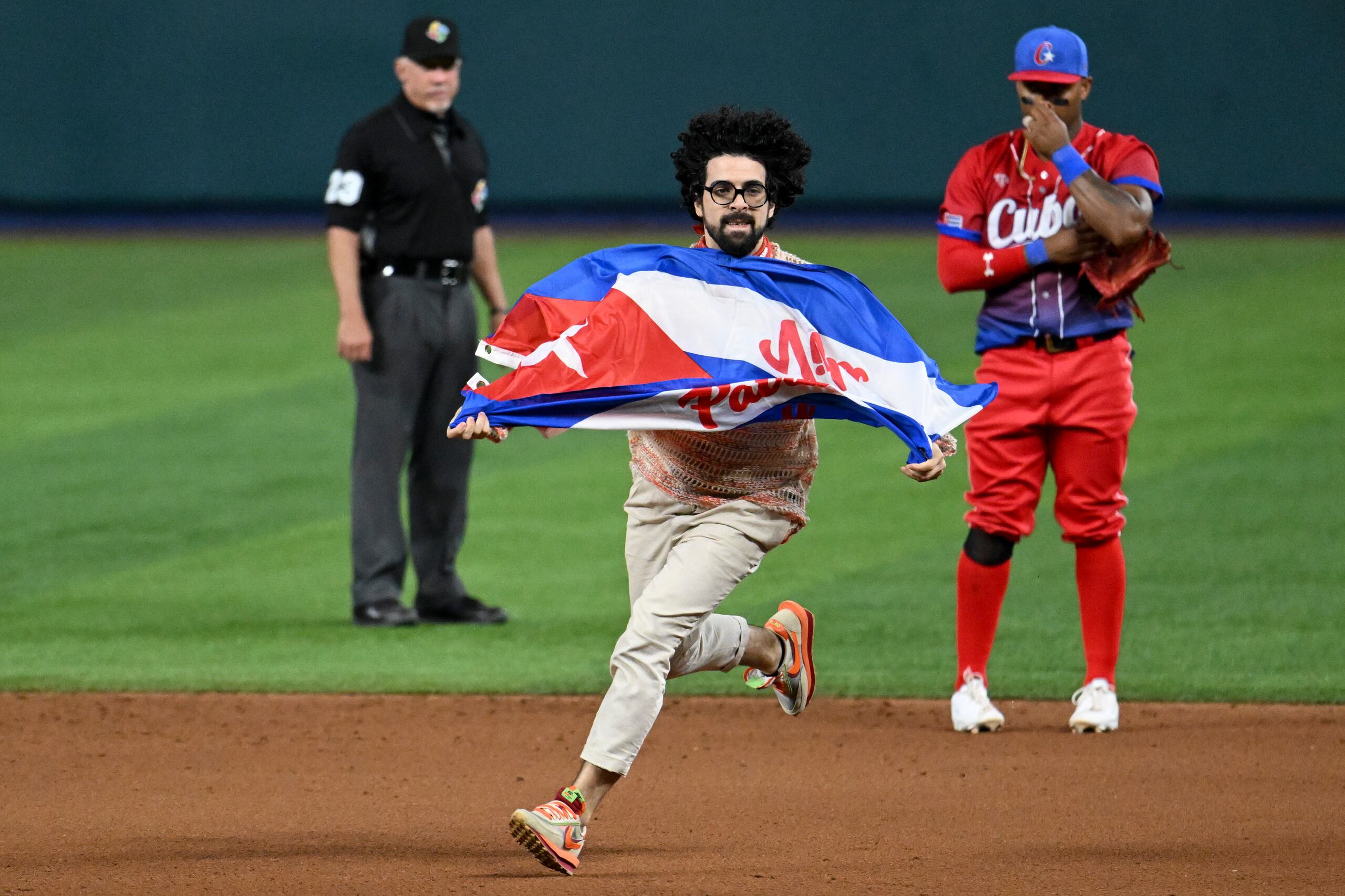 Un árbitro y un jugador cubano observan al hombre que entró con la bandera de Cuba.