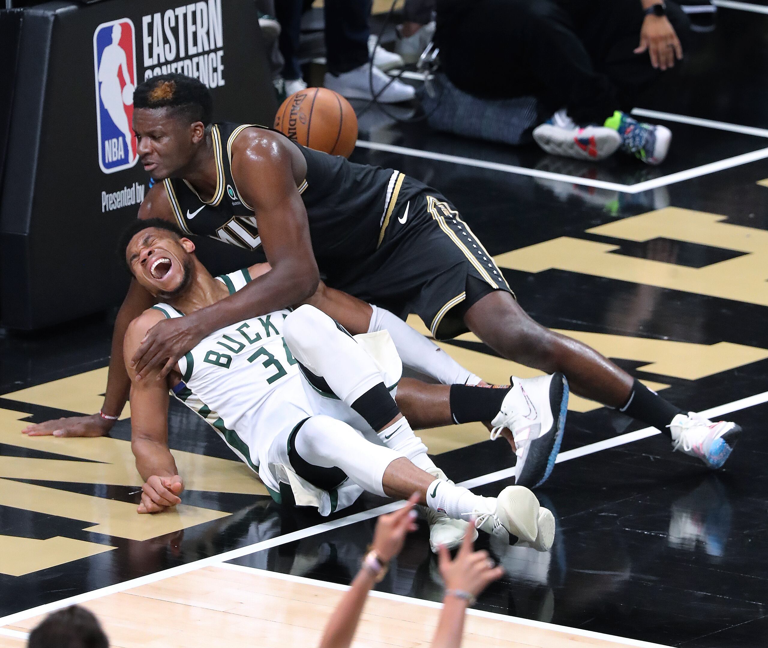 Giannis Antetokounmpo, de los Bucks, y Clint Capela, de los Hawks, caen al tabloncillo durante la jugada en que Antetokounmpo se lastimó la rodilla izquierda el martes.