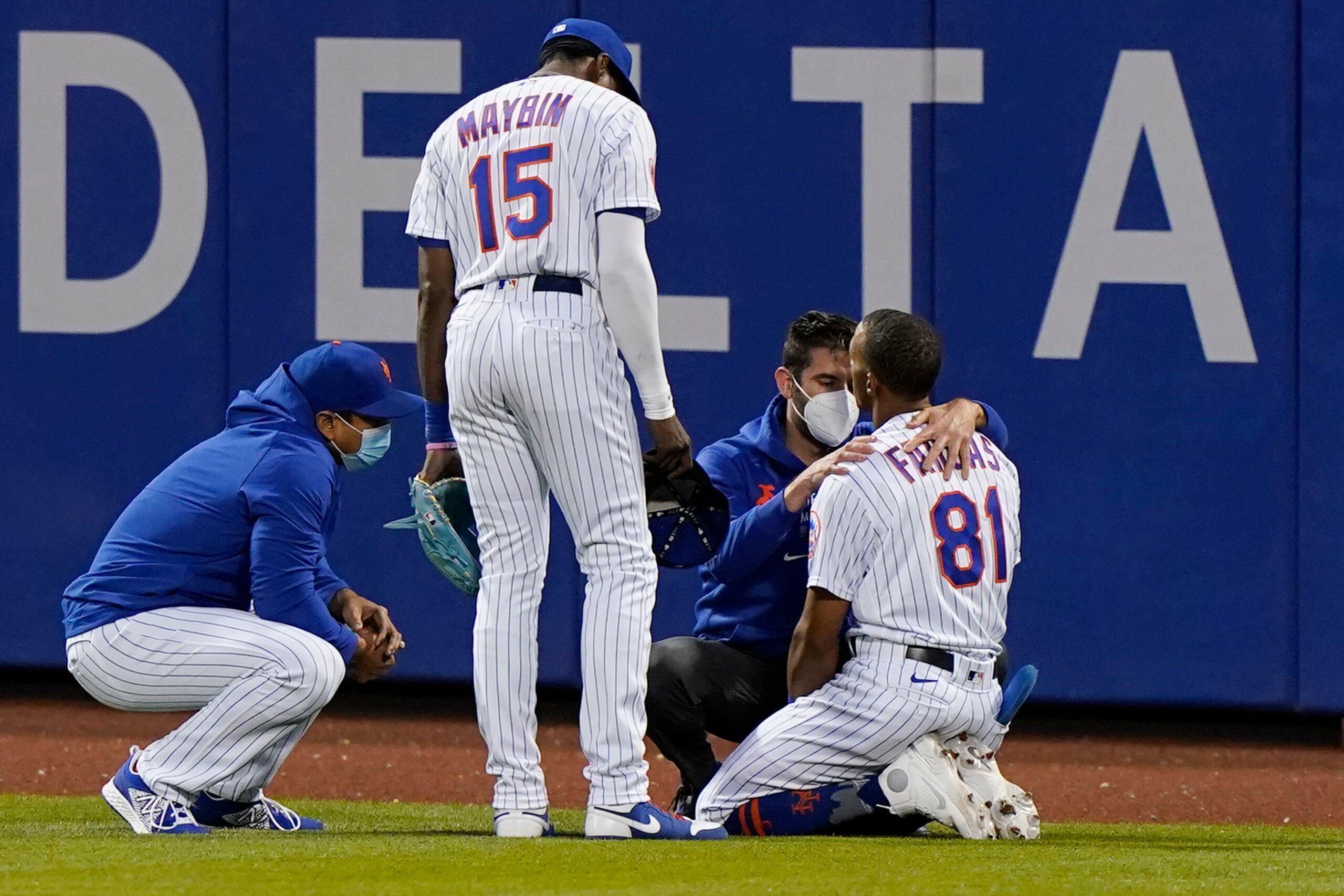 El dirigente Luis Rojas, a la izquierda, y el jardinero Cameron Maybin, observan mientras personal de los Mets revisa a Johneswhy Fargas tras su aparatoso choque contra la verja el lunes.