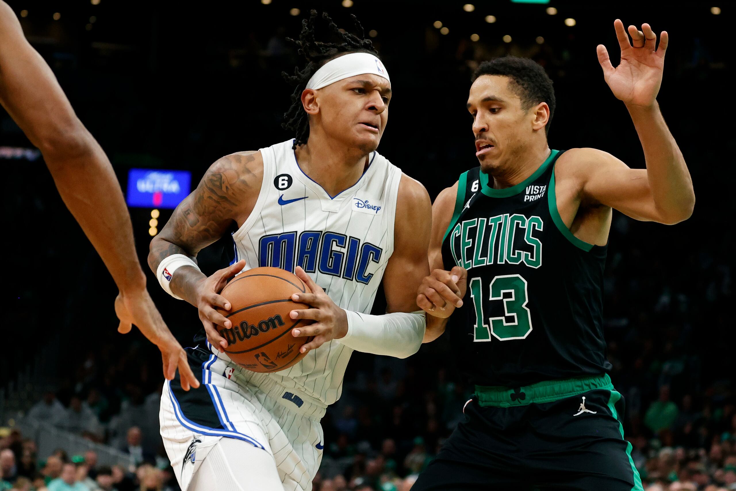 Paolo Banchero, izquierda, penetra ante la marca defensiva de Malcolm Brogdon (13), de los Celtics de Boston.