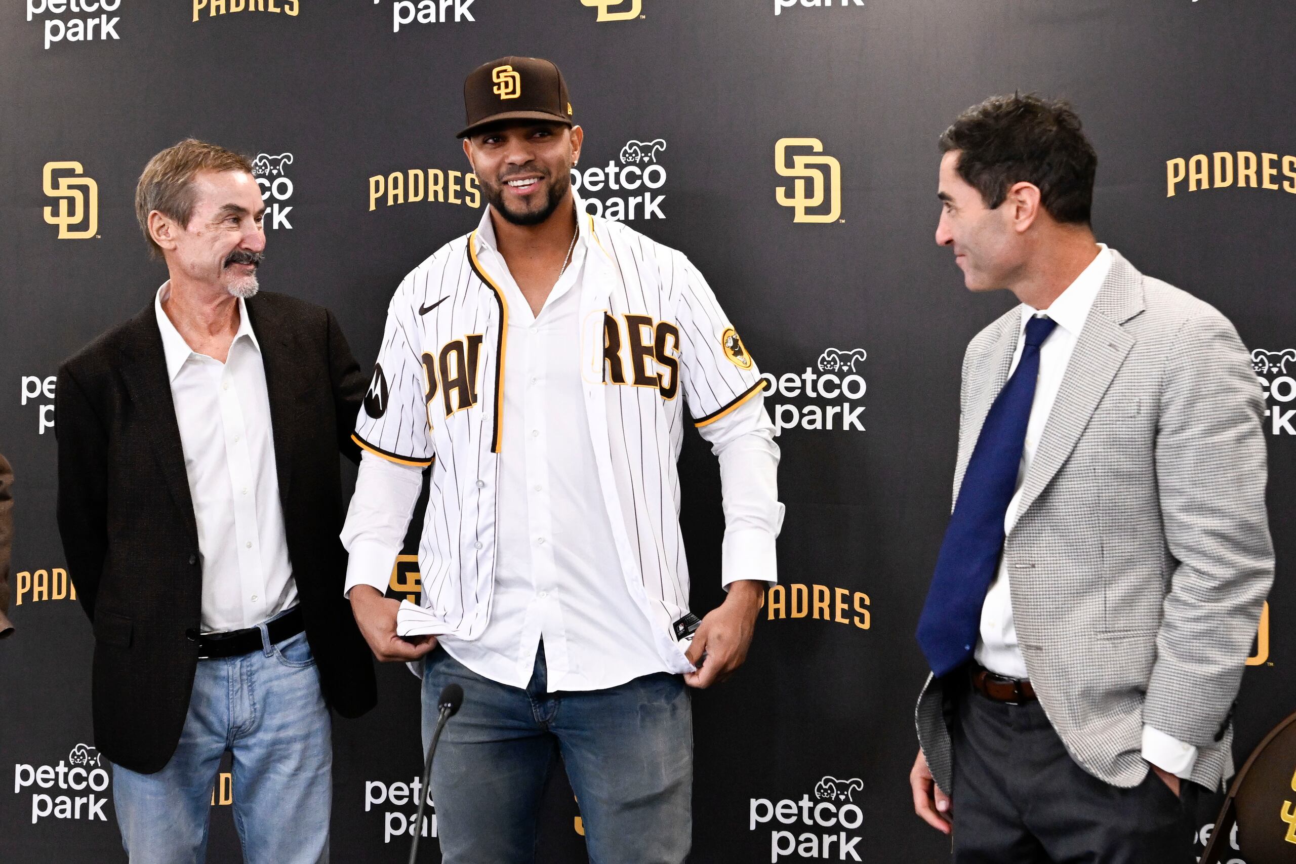 Xander Bogaerts, centro, se prueba el jersey de los Padres de San Diego, mientras A.J. Preller, gerente general, derecha, y Peter Seidler,  presidente de los Padres, le observa.