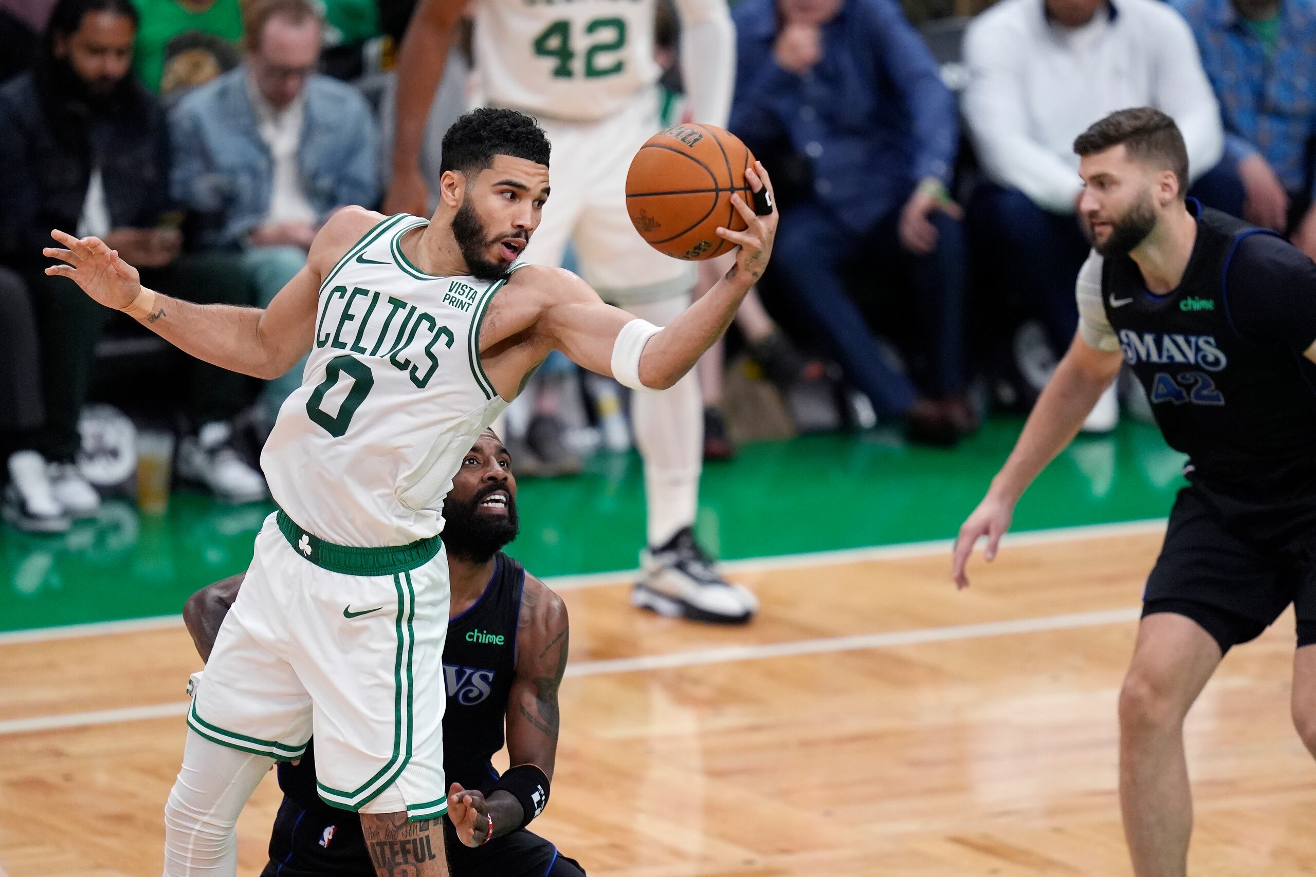 El alero de los Celtics de Boston, Jayson Tatum, y el base de los Mavericks de Dallas, Kyrie Irving, pelean por el balón frente a Maxi Kleber de los Mavs durante un instante de la acción del primer partido de la final.