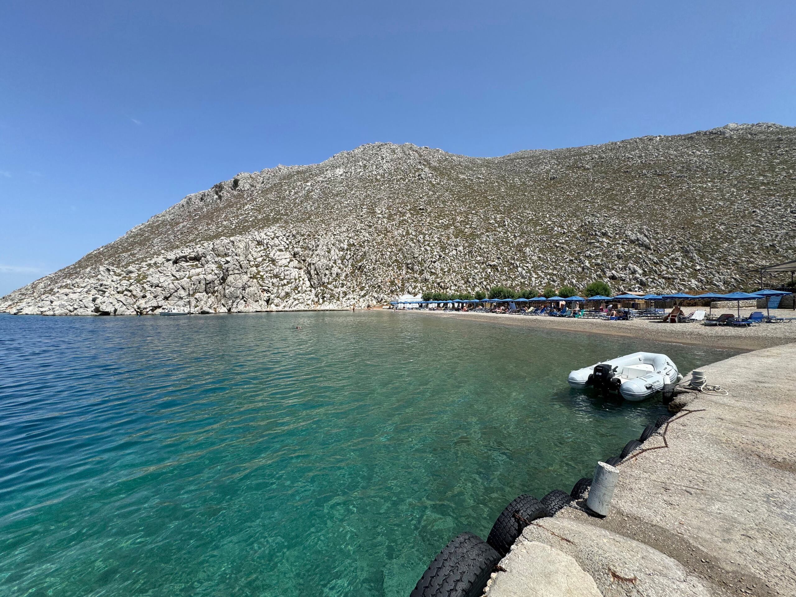 Gente sentada en la playa de Agios Nikolaos, en la zona de la que se cree salió el doctor y presentador de televisión británico Michael Mosley, en la isla de Symy, Grecia, en el sureste del mar Egeo.