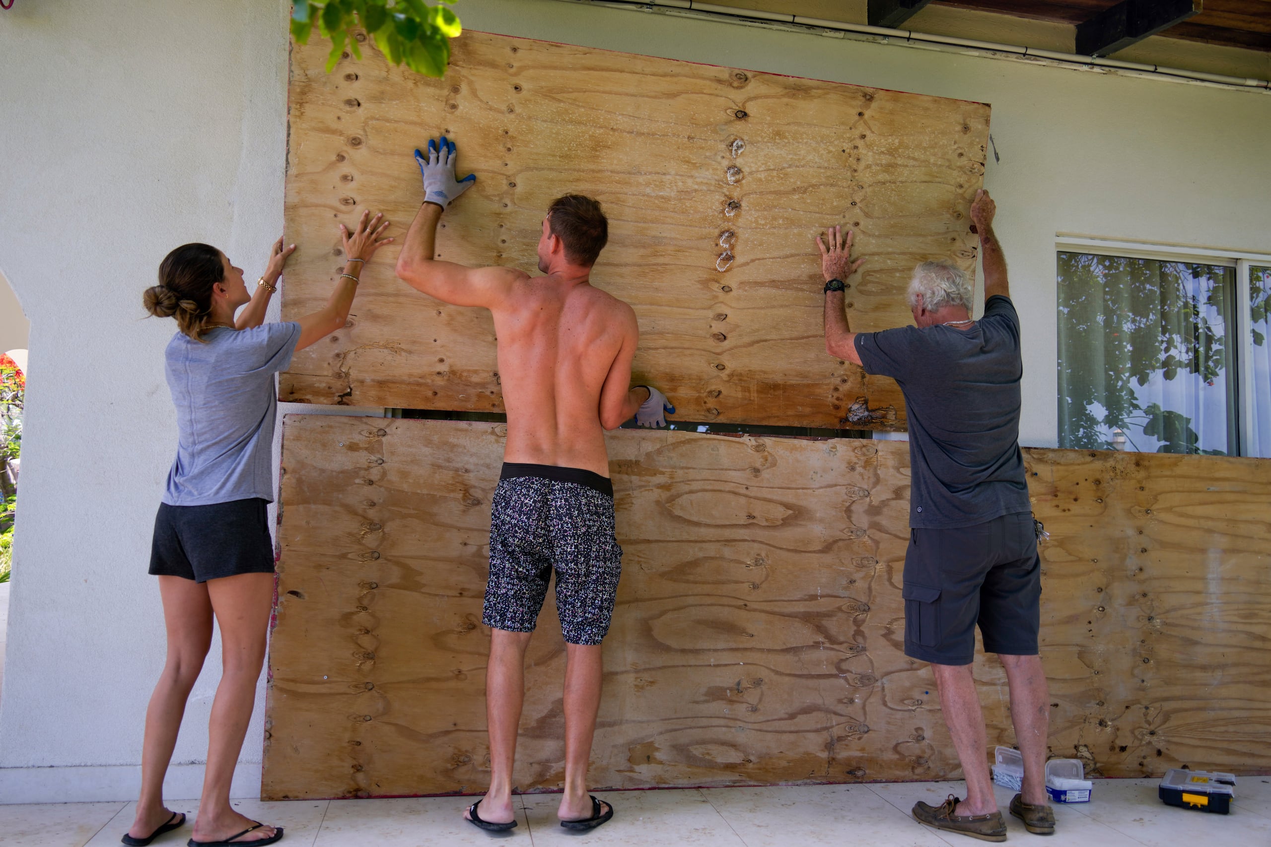 Tres personas cubren las ventanas de su hogar en preparación para la llegada del huracán Beryl el domingo 30 de junio de 2024, en Bridgetown, Barbados. (AP Foto/Ramón Espinosa)